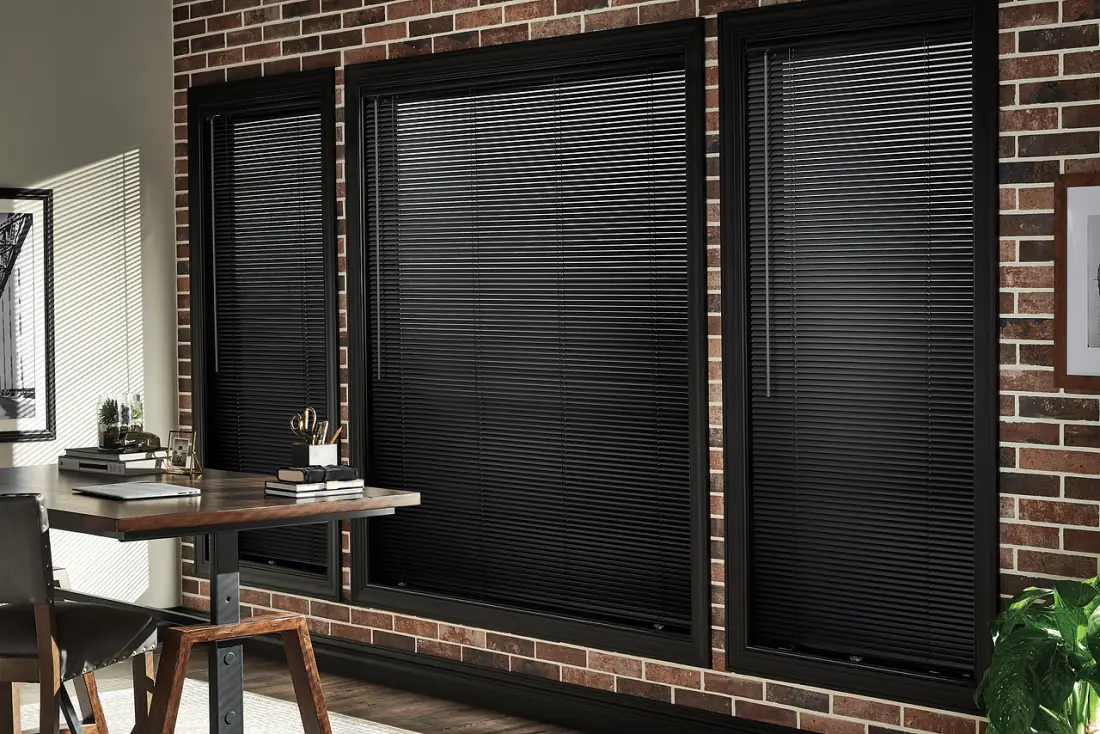 Black aluminum blinds covering large windows in a brick office with desk and chair in Venice, FL