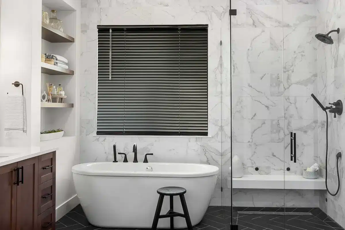 Black aluminum blinds above a freestanding bathtub in a marble-tiled bathroom with black fixtures in Venice, FL