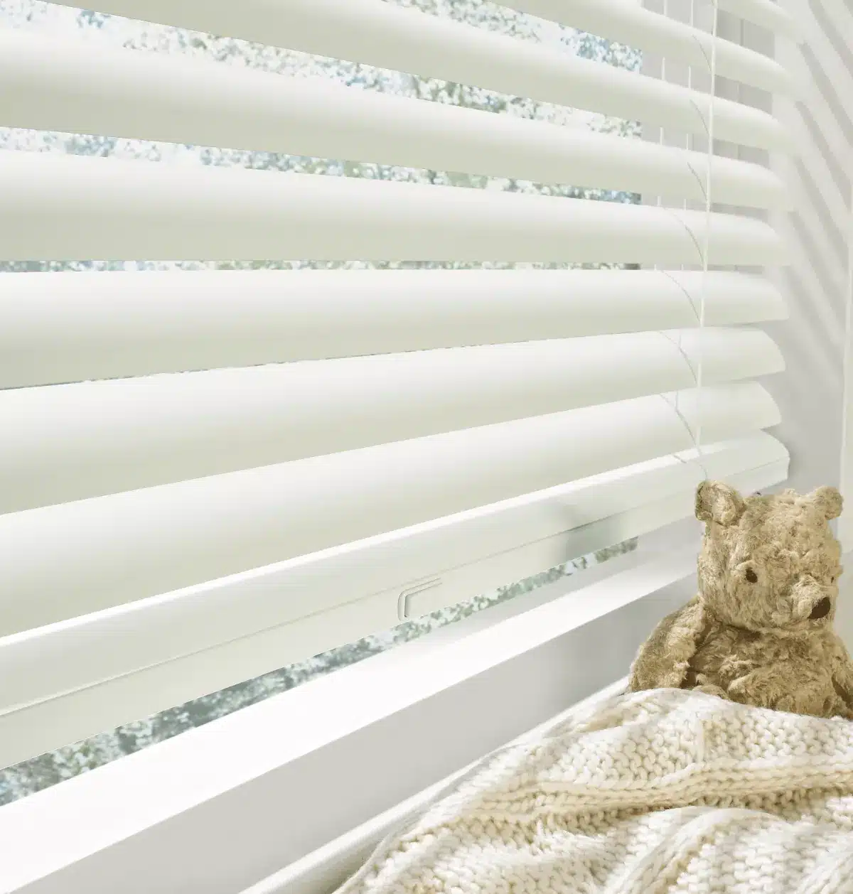 White blinds with patterned tape next to a teddy bear and cream blanket on a windowsill in Venice, FL