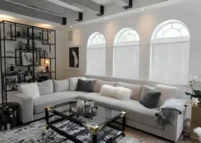 Modern living room with three arched windows dressed in white cellular shades and a light gray sectional sofa in Venice, FL