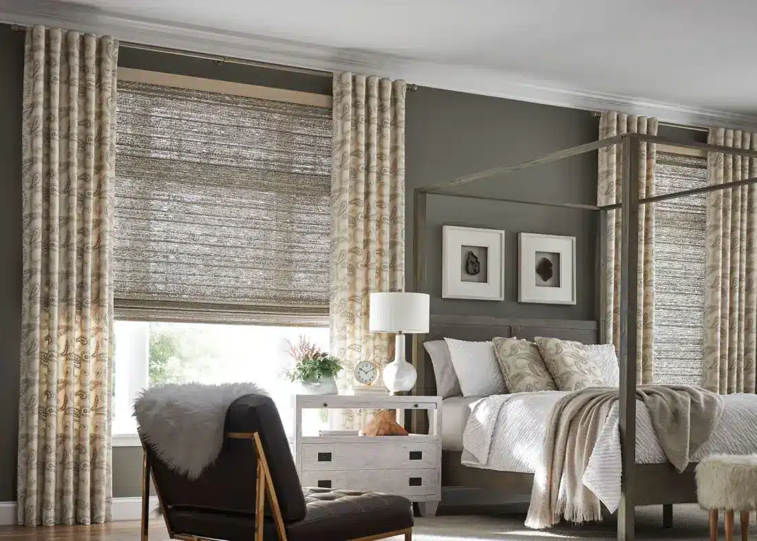 Elegant bedroom with cream patterned drapery panels flanking textured roman shades on large windows in Venice, FL