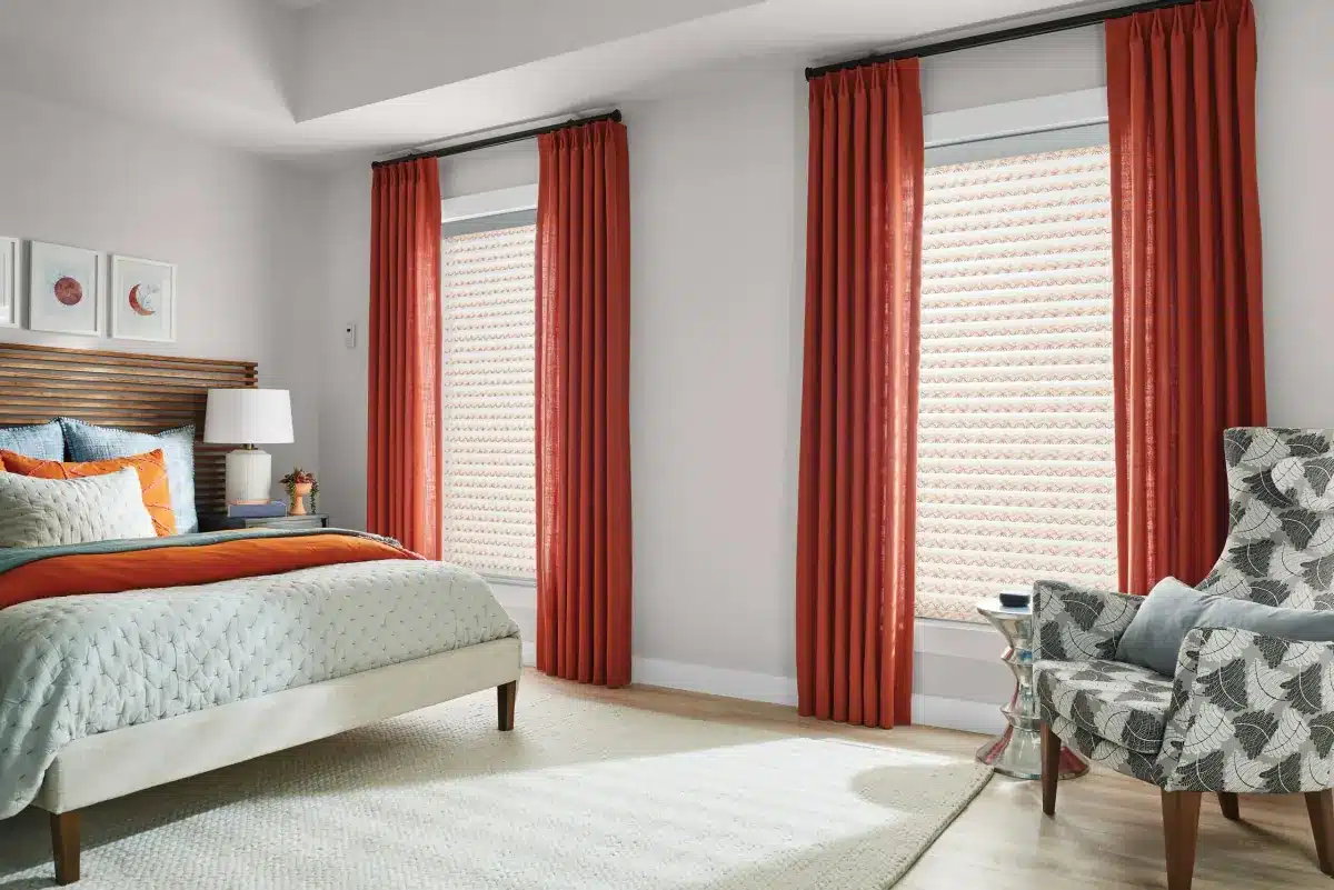 Red custom drapery panels frame large windows with woven shades in a modern bedroom in Venice, FL