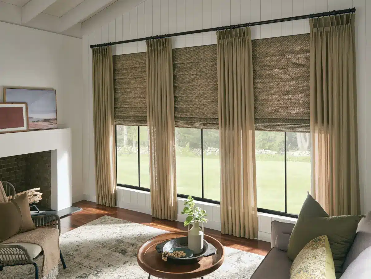 Elegant tan drapery with woven roman shades frames large windows overlooking green landscape in Venice, FL