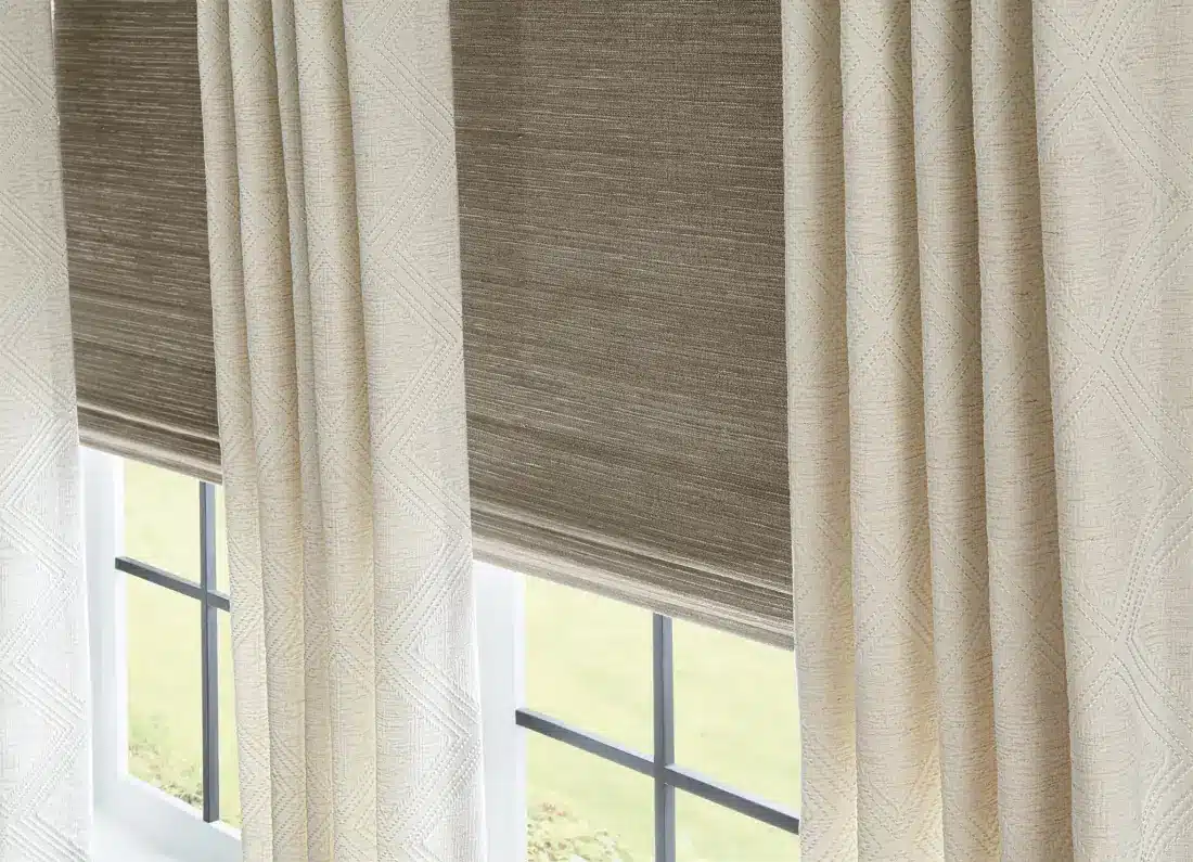 Cream drapery panels frame windows with coordinating woven roman shades and green outdoor view in Venice, FL