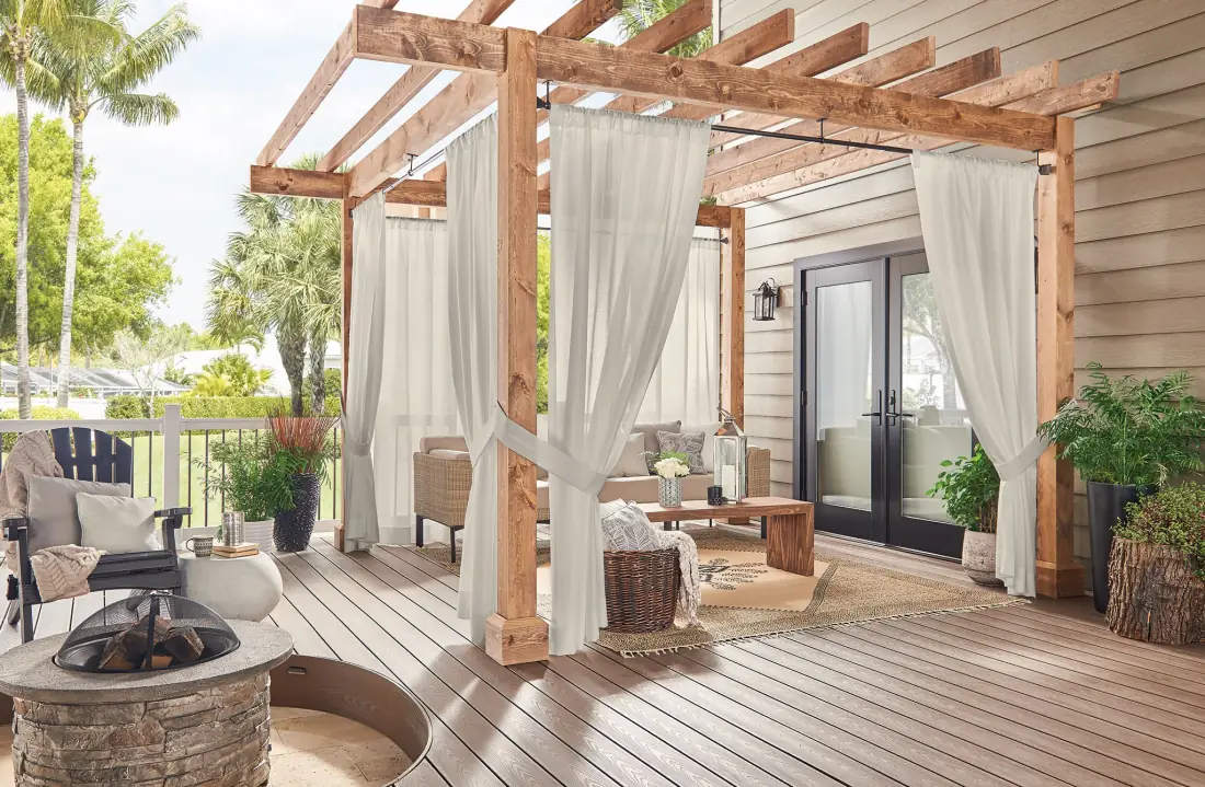 Cream drapery panels hang from a wooden pergola on a spacious outdoor patio adjacent to a residence in Venice, FL