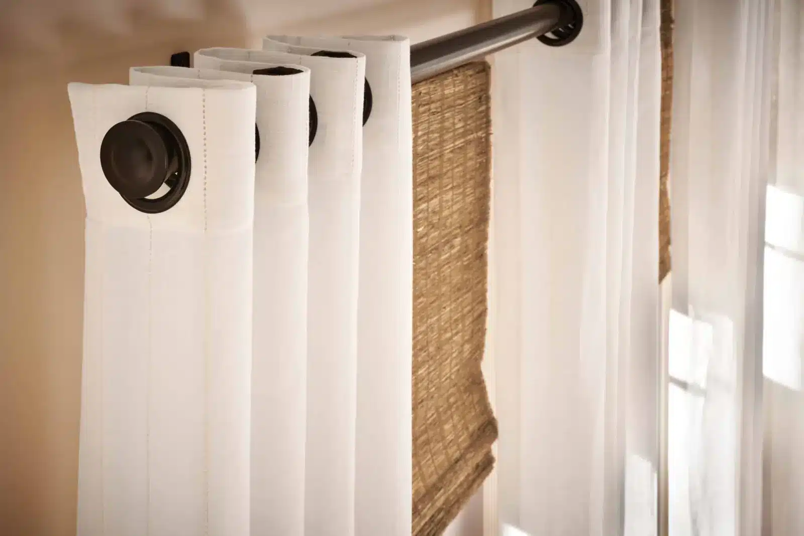 White grommet curtains layered with woven natural shades on a dark rod in Venice White grommet curtains layered with woven natural shades on a dark rod in Venice