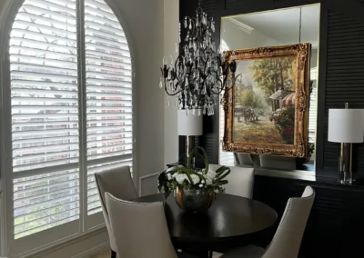 Arched plantation shutters frame a dining area with round black table and cream chairs in Venice, FL