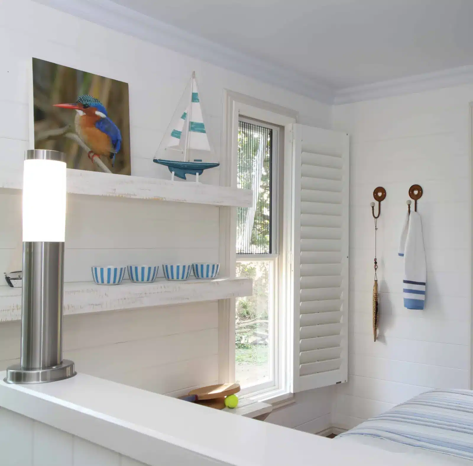 White plantation shutters frame a bright bathroom window with coastal decor and blue striped accents in Venice