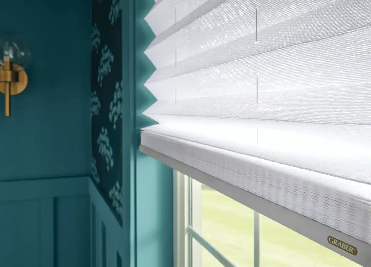 White pleated cellular shades installed on a window with teal wall trim and gold cross decoration in Venice, FL