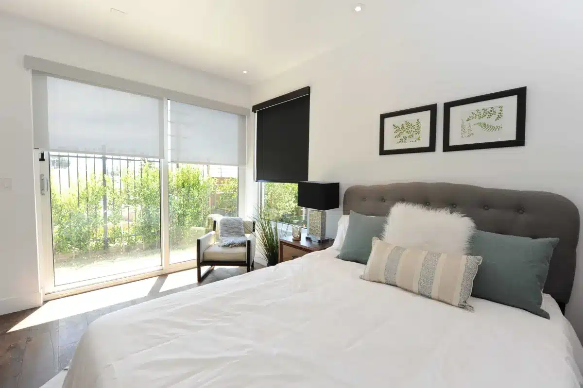 Modern bedroom with white roller shades on sliding glass doors opening to a balcony with green plants in Venice, FL