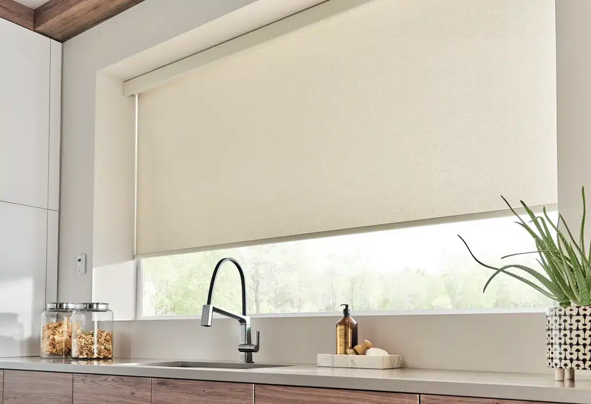 Cream roller shades partially lowered over a large kitchen window with natural outdoor view in Venice, FL