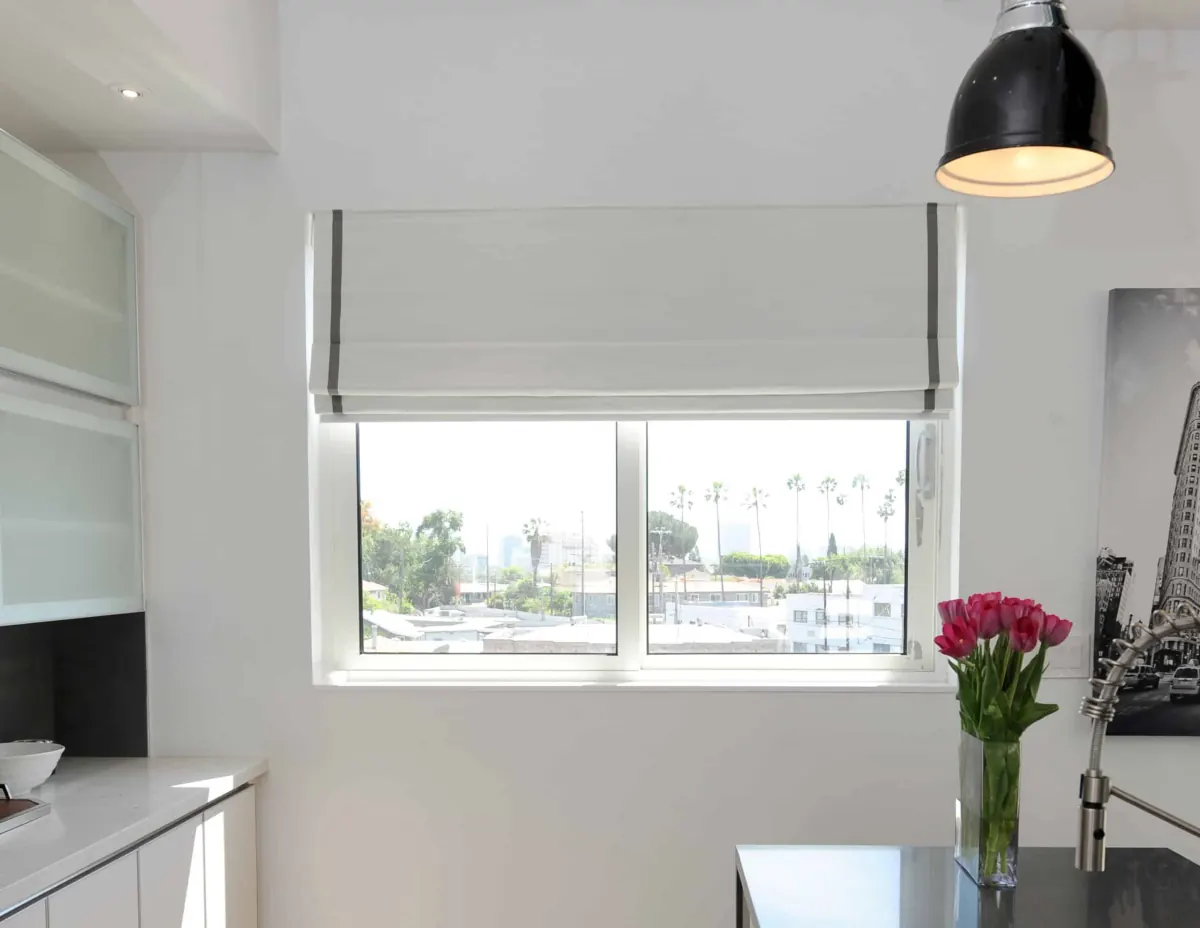 White roman shades with gray trim on large windows overlooking a sunny cityscape with palm trees in Venice, FL