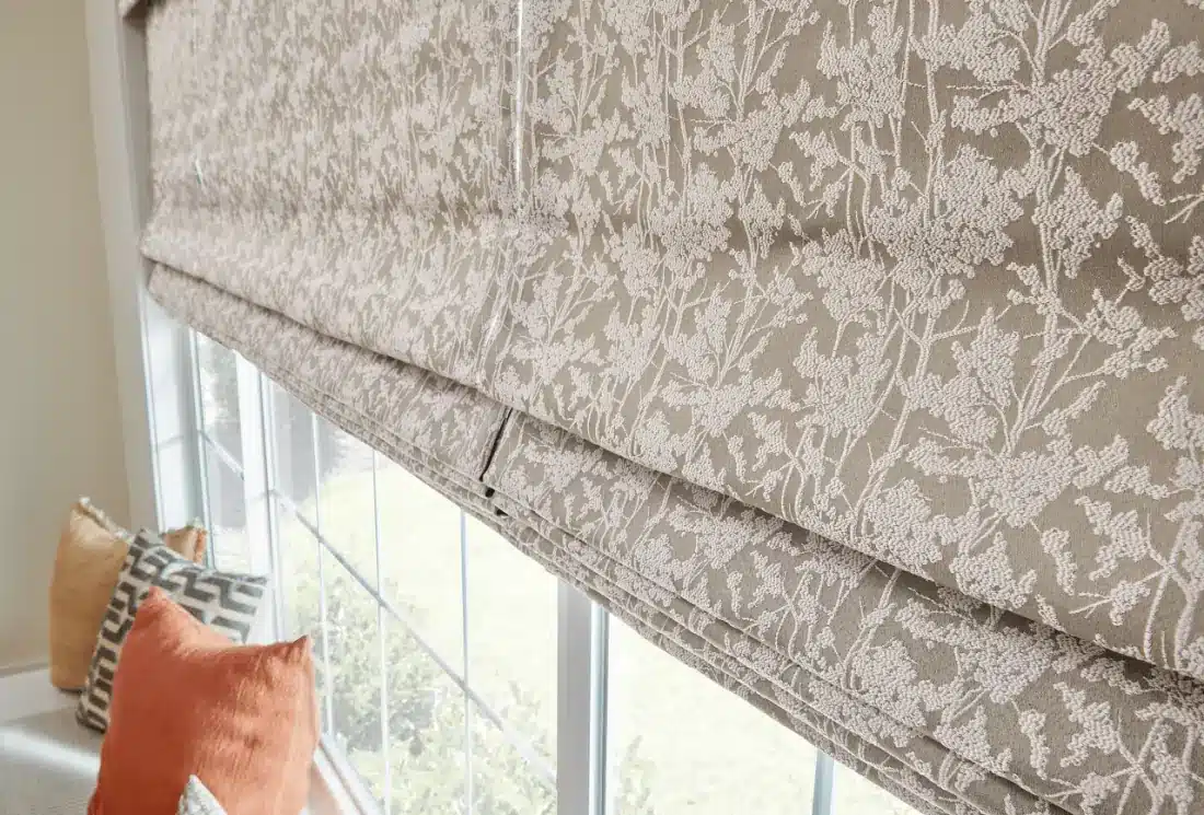 Tan roman shade with delicate floral pattern hung at a large window with garden view in Venice, FL