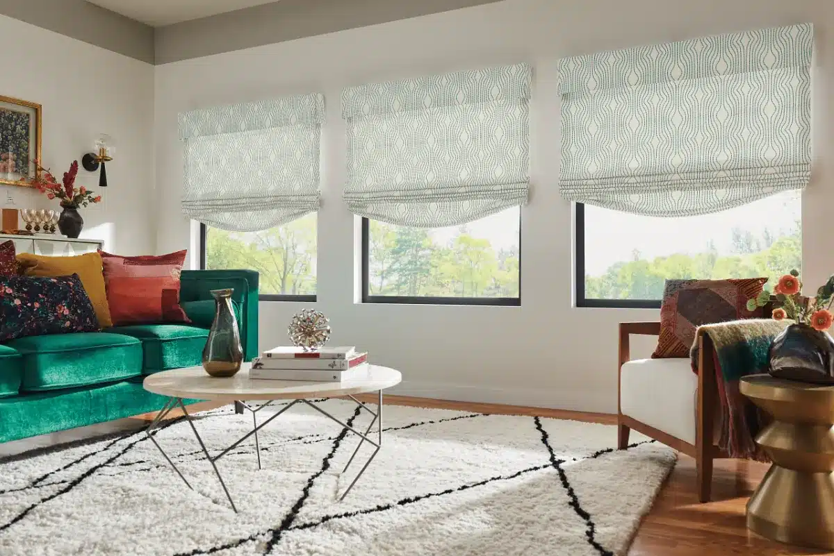 Three roman shades with geometric pattern hung above windows in a modern living room with green sofa in Venice, FL