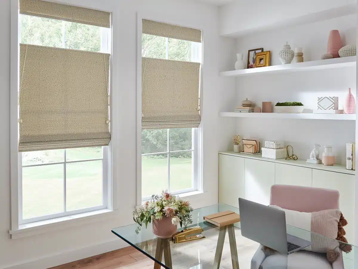 Natural woven roman shades on large windows above a modern home office desk with shelving in Venice