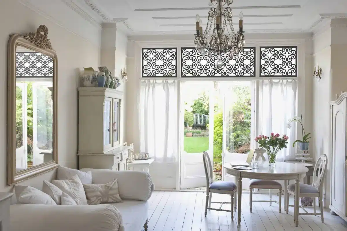 Bright sunroom with decorative black window grilles above sheer white drapery framing garden views in Venice, FL