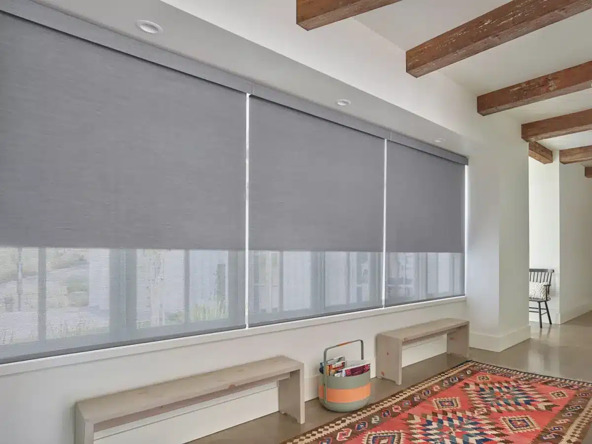 Gray solar shades with white dividers on large windows overlooking a natural landscape in a bright sunroom in Venice