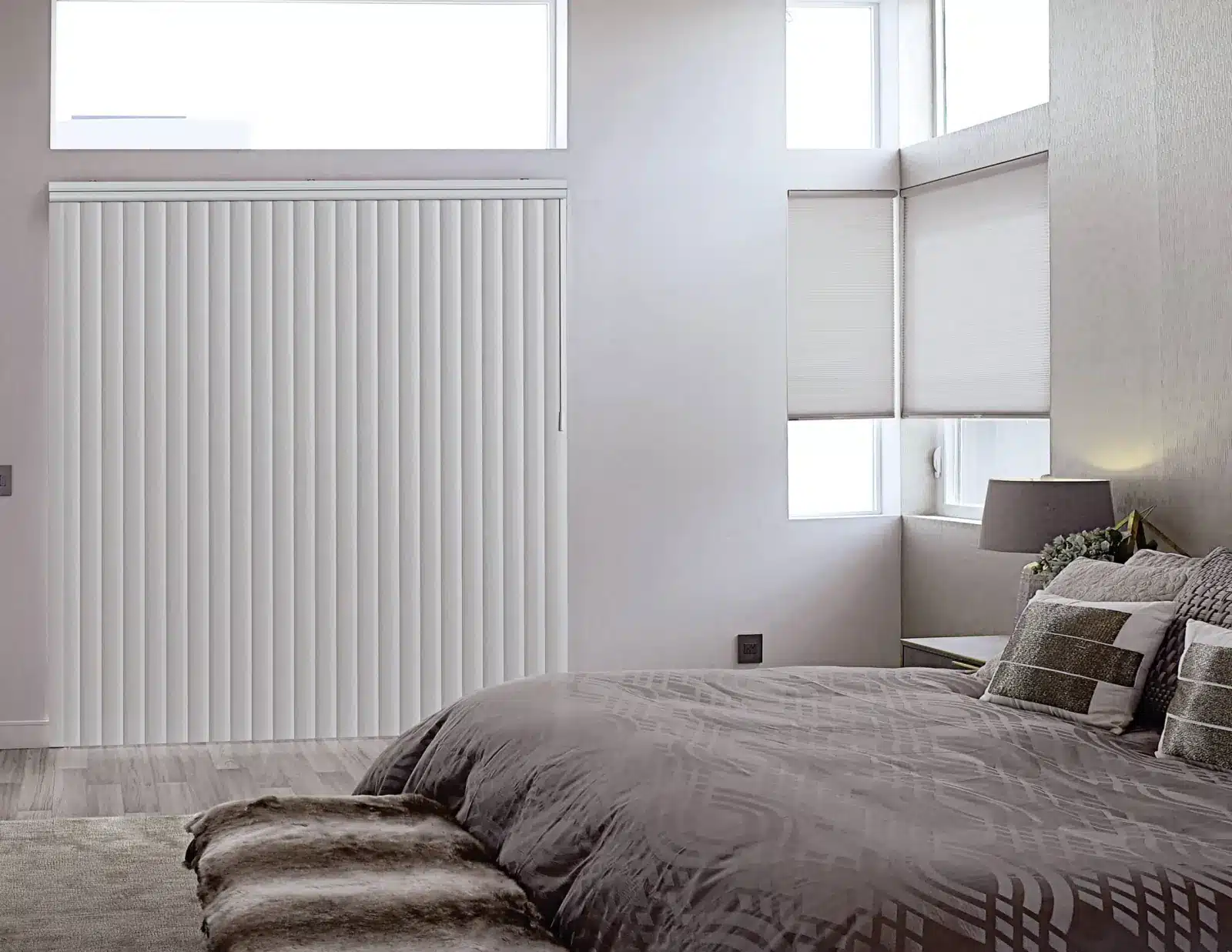 White vertical blinds cover sliding glass doors in a modern bedroom with gray bedding in Venice