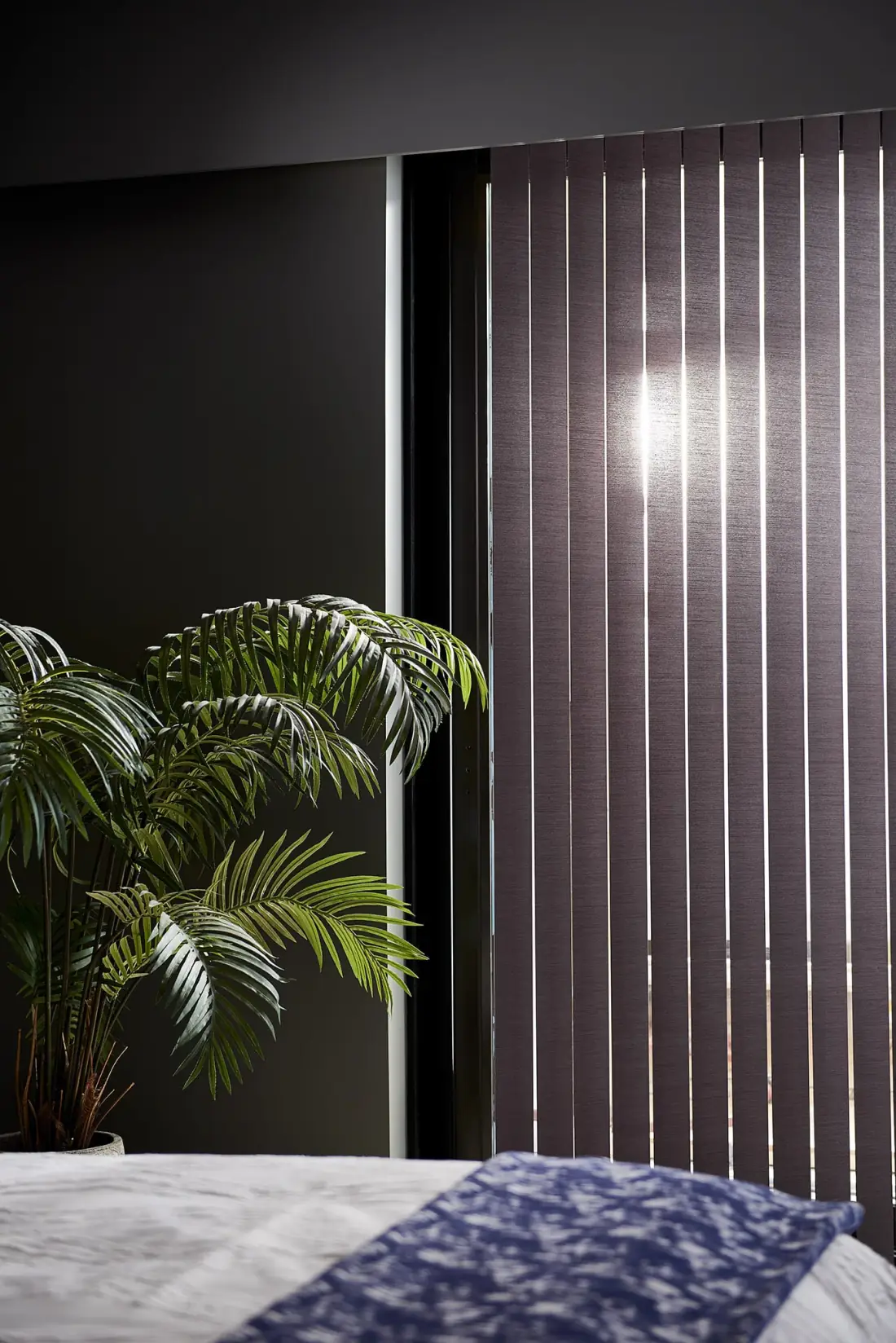 Charcoal vertical blinds with light filtering through slats beside a potted plant and bed in Venice, FL