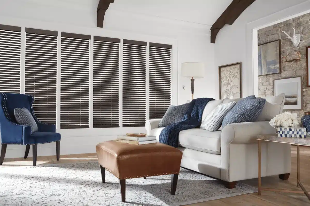 Black wood blinds covering large windows in a bright living room with beige sofa and blue accents in Venice, FL