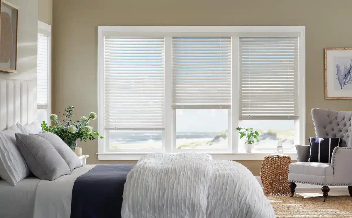 Bright bedroom with white faux wood blinds on large windows overlooking water and coastal landscape in Venice, FL