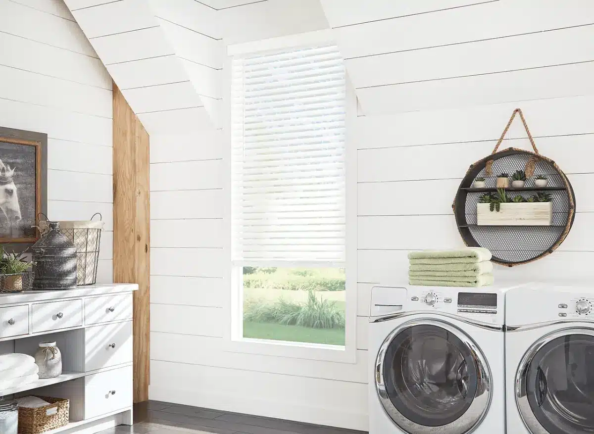 White faux wood blinds on a window in a bright laundry room with washing machines in Venice, FL