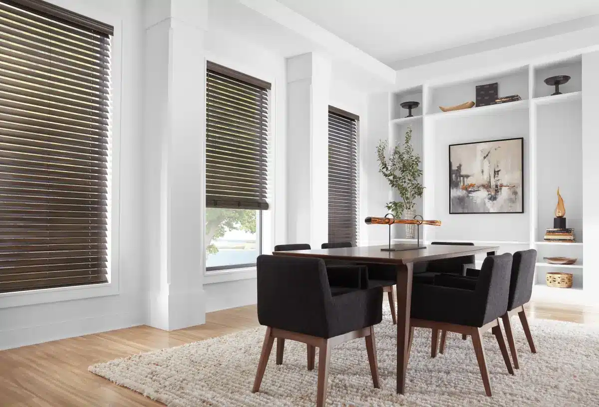 Dining room with bronze wood blinds on multiple windows overlooking water, with dark chairs and built-in shelving in Venice,
