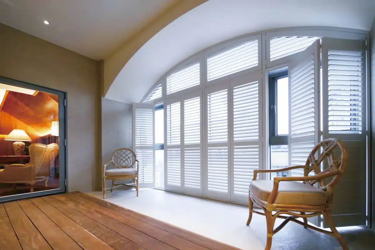 Bright sunroom with white plantation shutters on large arched windows and wooden chairs in Venice, FL