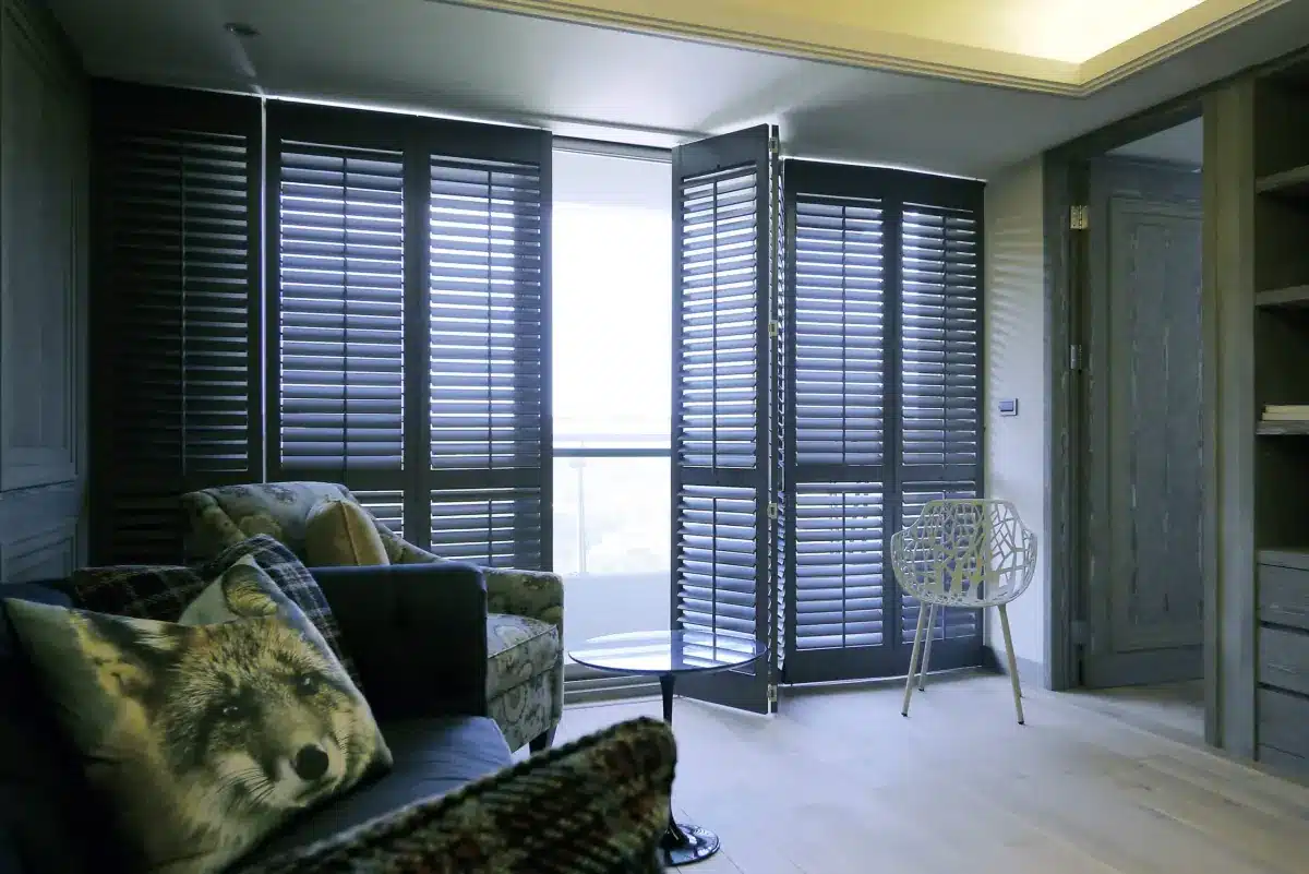 Black plantation shutters frame a bright balcony view in a modern sunroom with contemporary seating in Venice, FL