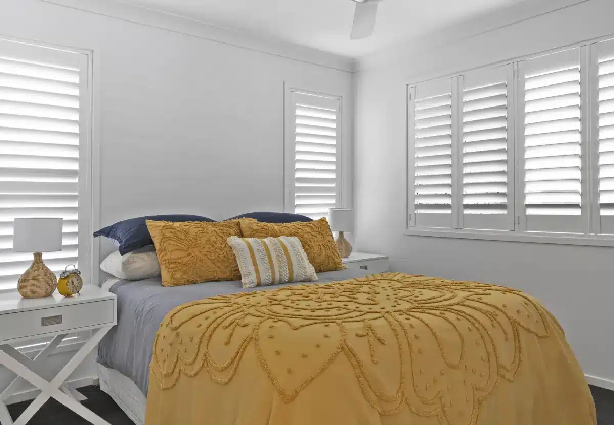 Bright bedroom with white plantation shutters on multiple windows and gold bedding in Venice, FL