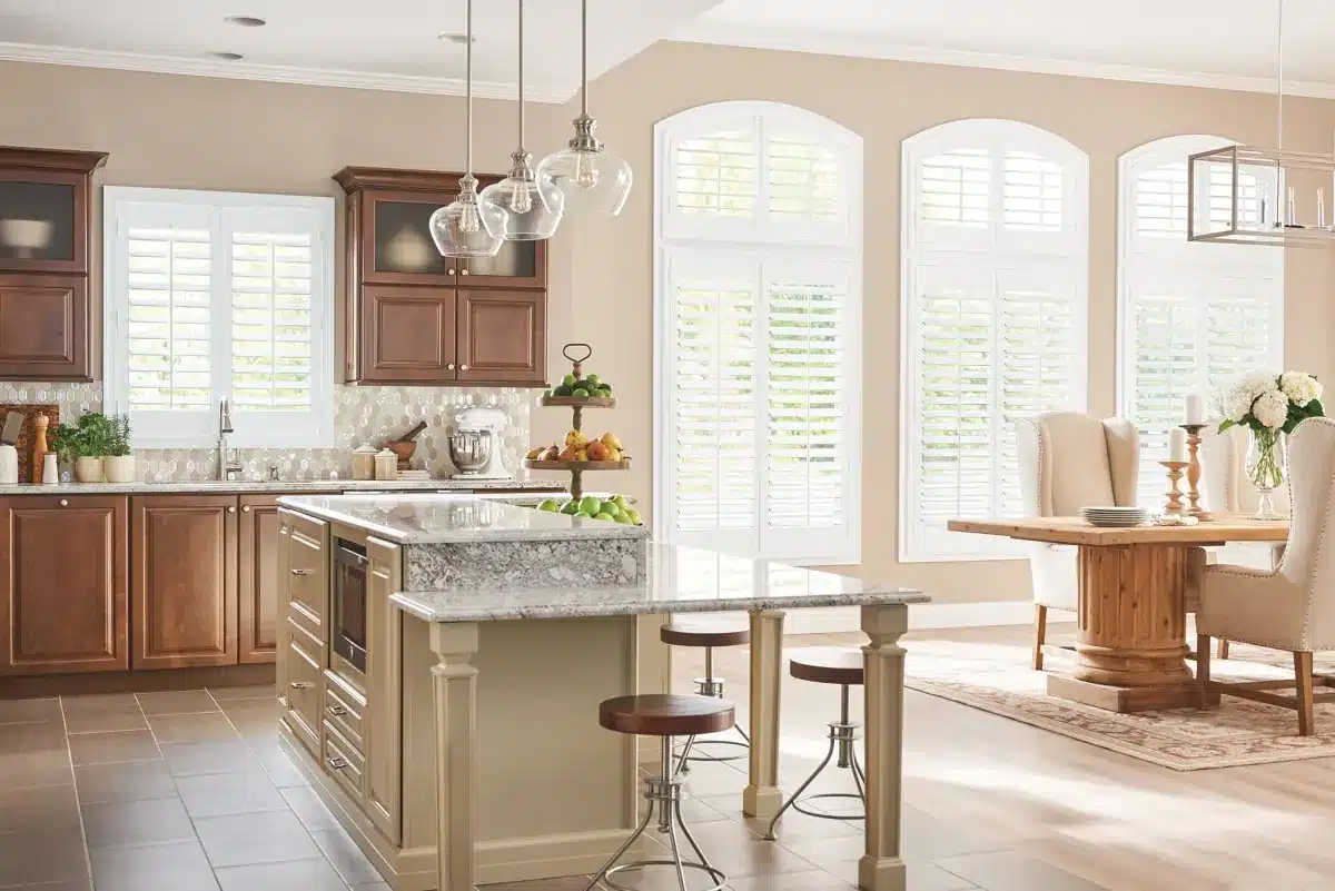 White plantation shutters frame arched windows in a bright kitchen and dining area with island seating in Venice, FL