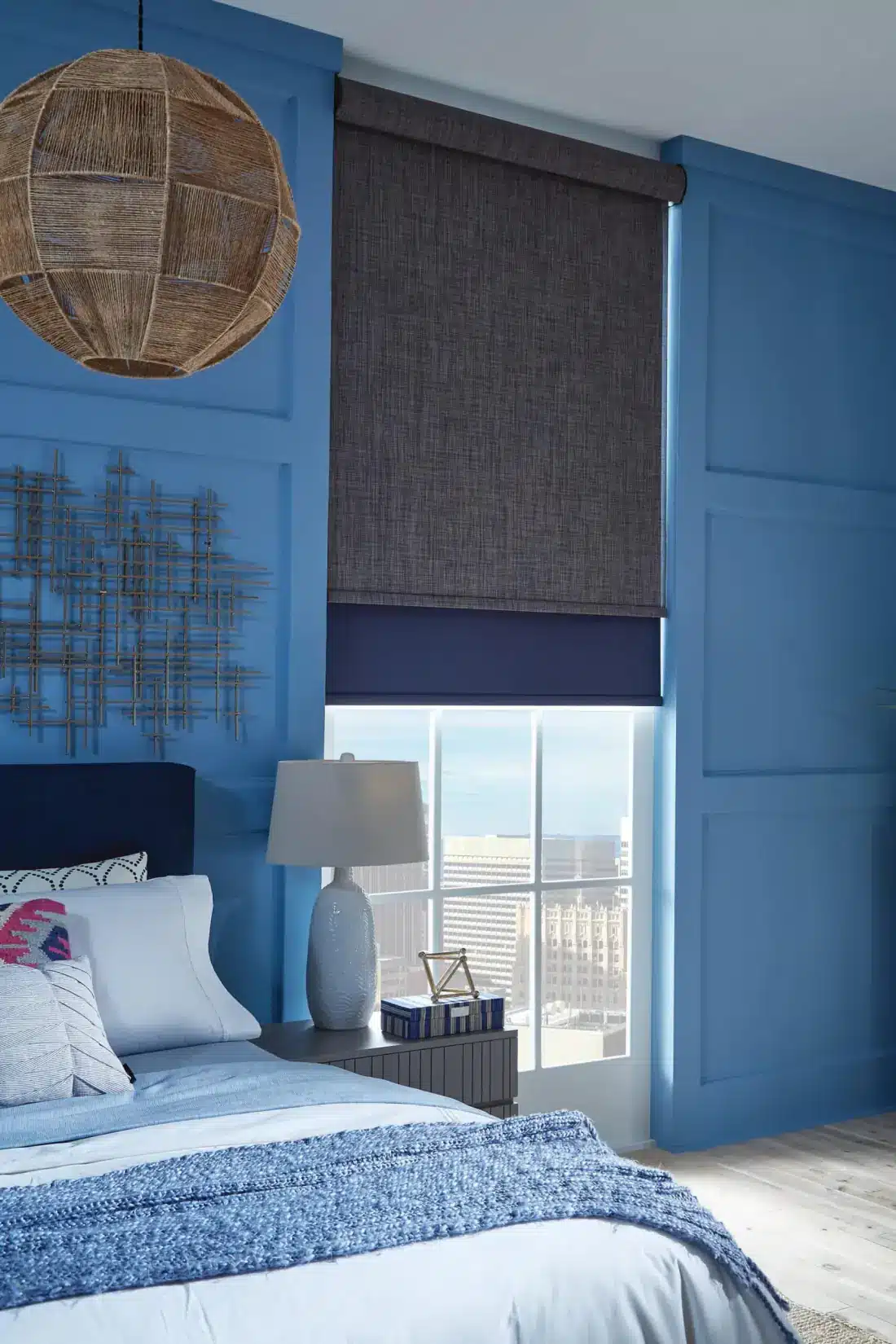 Woven roller shades in a modern bedroom with blue walls and city skyline views in Venice, FL