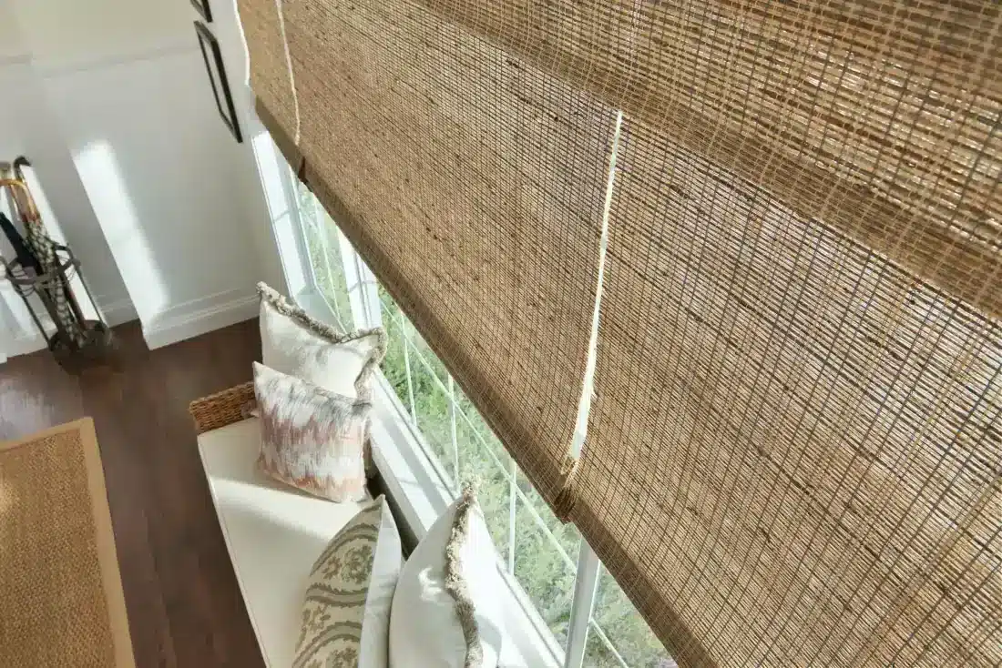 Woven wood shades in natural tan filtering light over a bright window seat with decorative pillows in Venice, FL